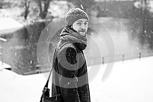 Outdoor portrait of handsome young man in snowy winter forest. Snowfall. Guy looking away on frozen river. Black and white