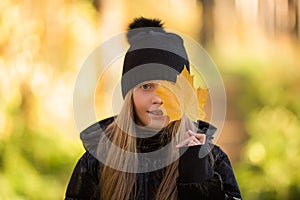 Outdoor portrait of happy blonde child girl holding yellow leaf. Little girl walking in the autumn park or forest. Warm sunny