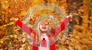 Outdoor portrait of happy blonde child girl in a red jacket holding yellow leaves. Little girl walking in the autumn park or