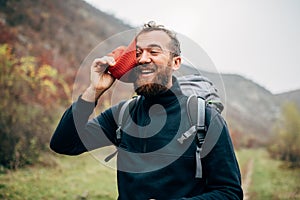 Outdoor portrait of happy hiker young man with red hat, hiking in mountains. Traveler bearded male smiling and feel happy