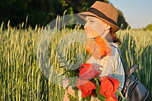 Outdoor portrait of happy mature woman with bouquets of red poppies flowers