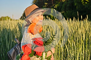 Outdoor portrait of a happy mature woman with bouquets of red poppies flowers