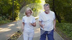 Outdoor portrait of happy senior man and woman jogging together in public park, enjoying jog workout in morning