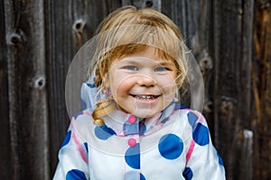 Outdoor portrait of happy smiling little toddler girl wearing rain jacket on rainy cloudy day. Cute healthy child in