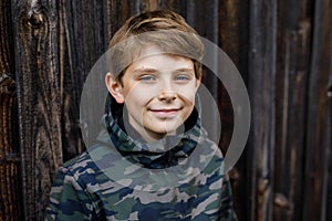 Outdoor portrait of happy smiling preteen kid boy wearing rain jacket on rainy cloudy day. Handsome healthy child in