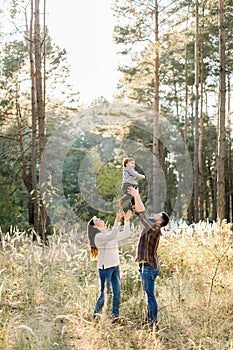 Outdoor portrait of happy young parents, having fun and lifting up their little cute baby son, during walk in autumn