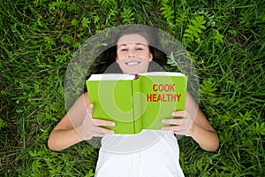 Outdoor portrait of a happy young woman reading a cookbook