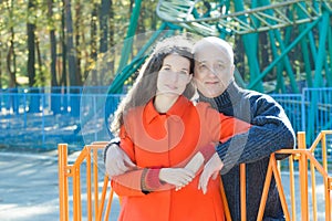 Outdoor portrait of hugging adult daughter and her senior father at roller coaster amusement park background