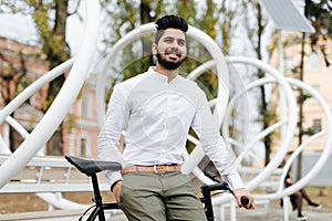 Outdoor portrait of indian young man sitting on bike with mobile phone in the street