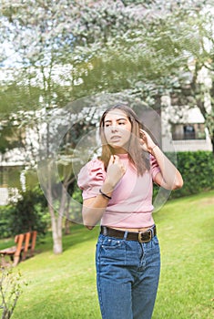 Outdoor portrait of a Latina teenage girl adjusting her straight hair with her hands in pink blouse and jeans