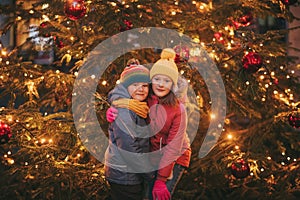 Outdoor portrait of little children next to Christmas tree with lights