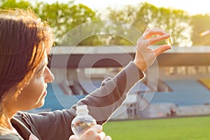 Outdoor portrait of mature woman taking vitamin E capsule pill of cod liver oil, at the stadium.