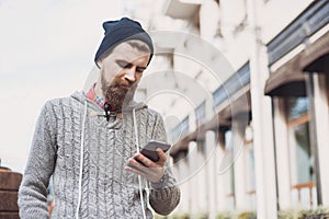 Outdoor portrait of modern young traveler man using smart phone on the street