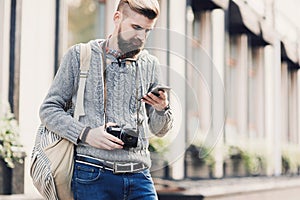 Outdoor portrait of modern young traveler man using smart phone on the street