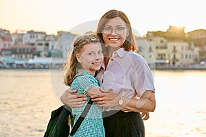 Outdoor portrait of mom and daughter 10, 11 years old on the sunset city sea promenade