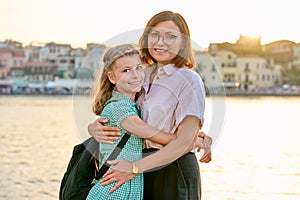 Outdoor portrait of mom and daughter 10, 11 years old on the sunset city sea promenade