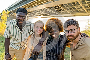 Outdoor portrait of multicultural group of four people looking at camera and smiling. Togetherness and bonding in