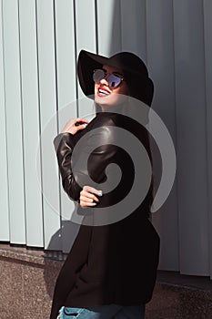 Outdoor portrait of pretty brunette woman in fashionable outfit, wears hat and glasses, posing in sun light