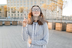 Outdoor portrait of smart teenager girl with glasses showing index finger up idea, eureka, golden hour