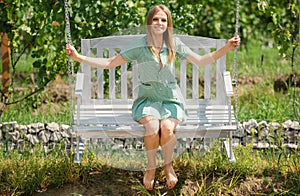 Outdoor portrait of a smiling happy girl. Young woman on swing relax at nature garden. Outdoor portrait of a smiling