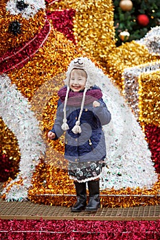 Outdoor portrait of smiling little girl in christmas decorations on street of european city. Winter and Christmas holidays concept