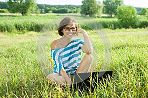 Outdoor portrait smiling middle-aged woman freelancer blogger traveler with laptop on nature