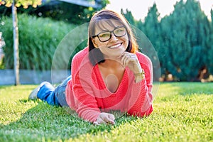 Outdoor portrait of smiling middle aged woman lying on grass