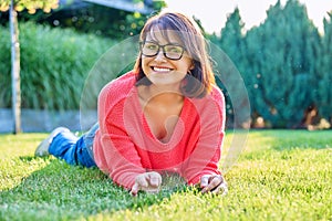 Outdoor portrait of smiling middle aged woman lying on grass