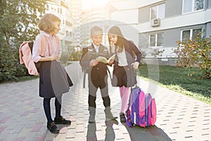 Outdoor portrait of smiling schoolchildren in elementary school. Group of kids with backpacks are having fun, talking, reading a