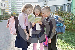 Outdoor portrait of smiling schoolchildren in elementary school. Group of kids with backpacks are having fun, talking, reading a