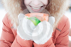Outdoor portrait of a smiling young girl in a fur hood. Drinking