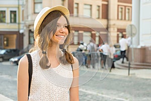 Outdoor portrait of teenage girl 13, 14 years old, city street background. Romantic smiling beautiful girl in a hat looks away, co