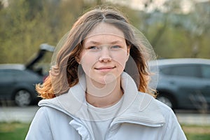 Outdoor portrait of teenager girl 15 years old, girl smiling with long brown hair in white jacket