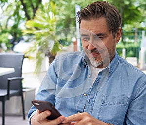 Outdoor portrait of white man using phone on a terrace, checking e-mails, reading news feed, posting on social media