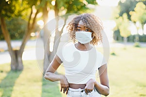 An outdoor portrait of a young African female with chestnut braids and in a virus protective mask on her face; masked black woman