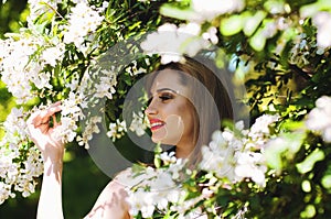 Outdoor portrait of young attractive woman in garden of blooming apple trees. Woman's Day. Female spring concept.