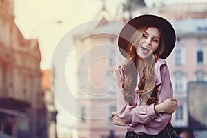 Outdoor portrait of young beautiful fashionable happy lady posing on the street. Model wearing stylish wide-brimmed hat