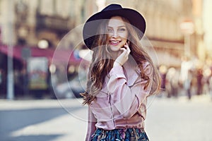 Outdoor portrait of young beautiful fashionable happy lady posing on the street. Model wearing stylish wide-brimmed hat