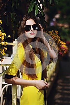 Outdoor portrait of young beautiful fashionable lady posing on street. Model wearing sunglasses and stylish yellow