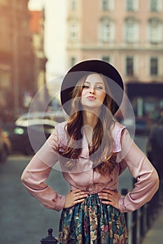 Outdoor portrait of young beautiful fashionable playful lady posing on old street. Model wearing stylish hat and clothes