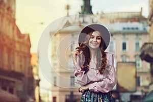 Outdoor portrait of young beautiful fashionable smiling lady posing on old street. Model wearing stylish hat and clothes