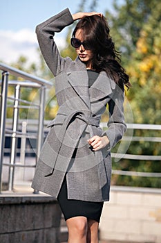 Outdoor portrait of a young beautiful fashionable woman, outdoors. A model dressed in a stylish gray coat, sunglasses. The concept