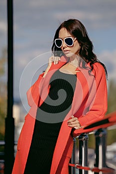 Outdoor portrait of a young beautiful fashionable woman, outdoors. The model, dressed in a stylish orange coat