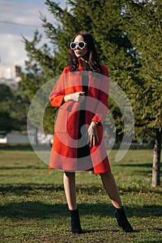 Outdoor portrait of a young beautiful fashionable woman, outdoors. The model, dressed in a stylish orange coat, sunglasses. The co