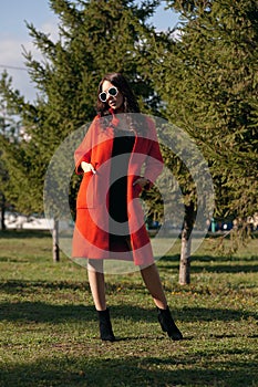 Outdoor portrait of a young beautiful fashionable woman, outdoors. The model, dressed in a stylish orange coat, sunglasses. The co