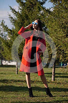 Outdoor portrait of a young beautiful fashionable woman, outdoors. The model, dressed in a stylish orange coat, sunglasses. The co