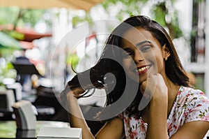 Outdoor portrait of young beautiful girl 19 to 25 years. Brunette. sitting in a restaurant outdoors. Wearing a fresh floral dress