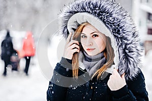 Outdoor portrait of young beautiful girl wearing in black jacket with a hood . Model posing in street. Winter holidays concept