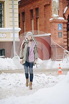 Outdoor portrait of young beautiful happy girl posing on street. Model wearing stylish warm clothes. Magic snowfall. Winter holida