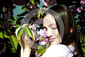 Outdoor portrait of young beautiful happy smiling lady posing near flowering tree.